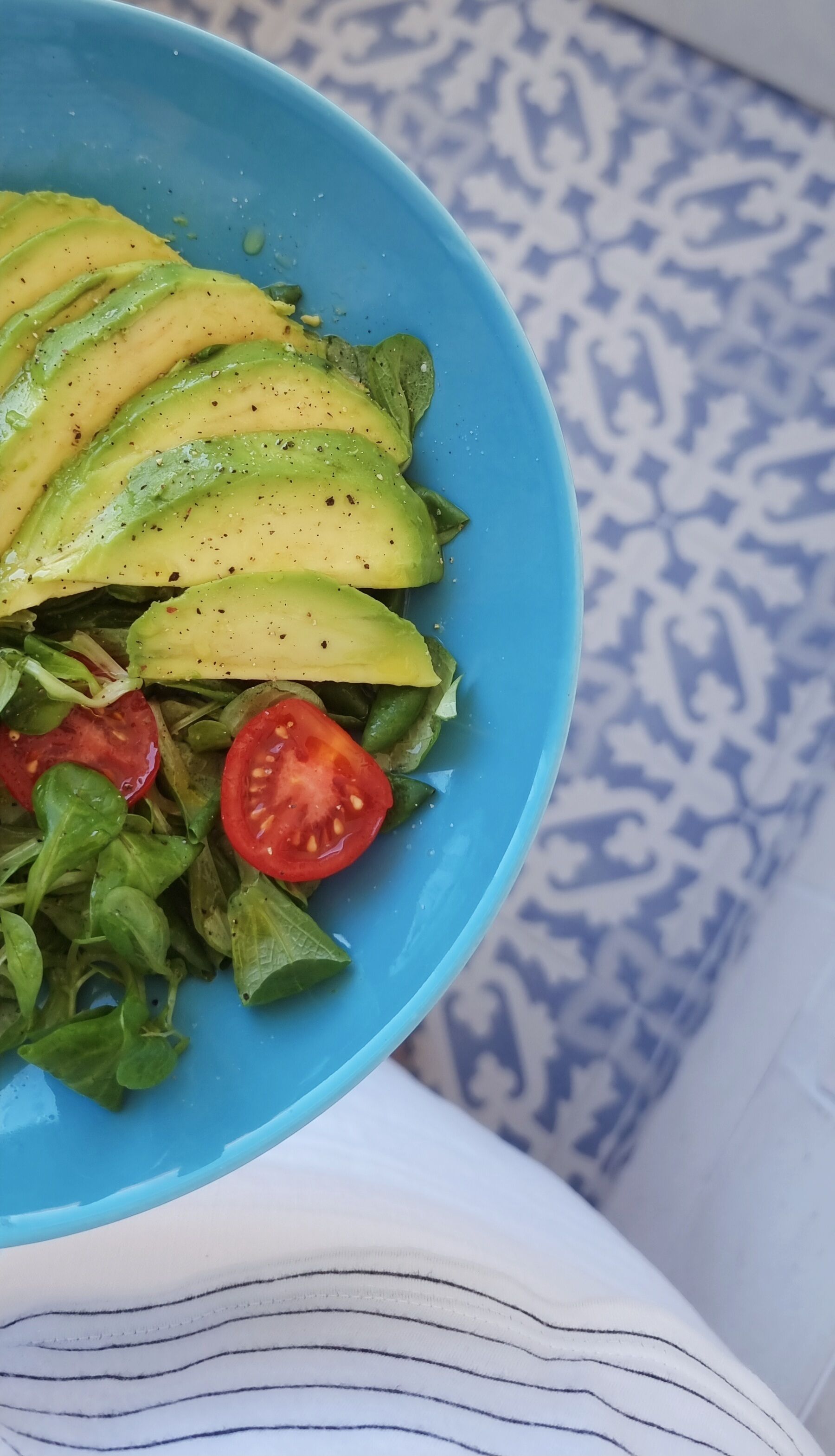 A blue bowl containing a salad with avocado slices, tomatoes, and greens.