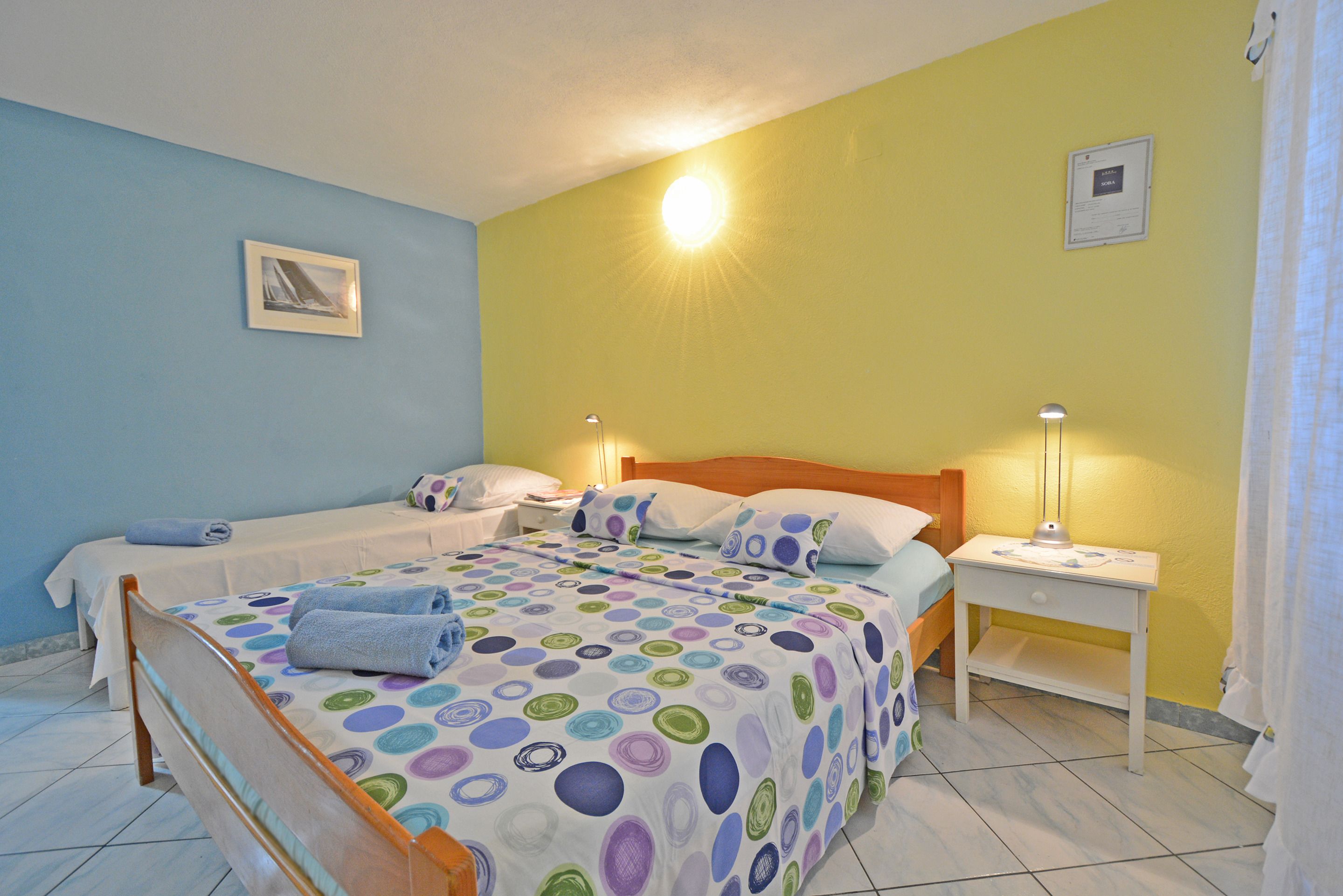 A bedroom with two beds, a nightstand, and a wall-mounted lamp.