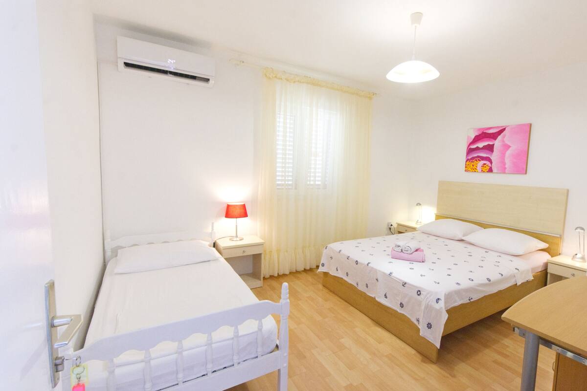 Een kamer met twee bedden, een bureau, een stoel, een airconditioning en een schilderij aan de muur.