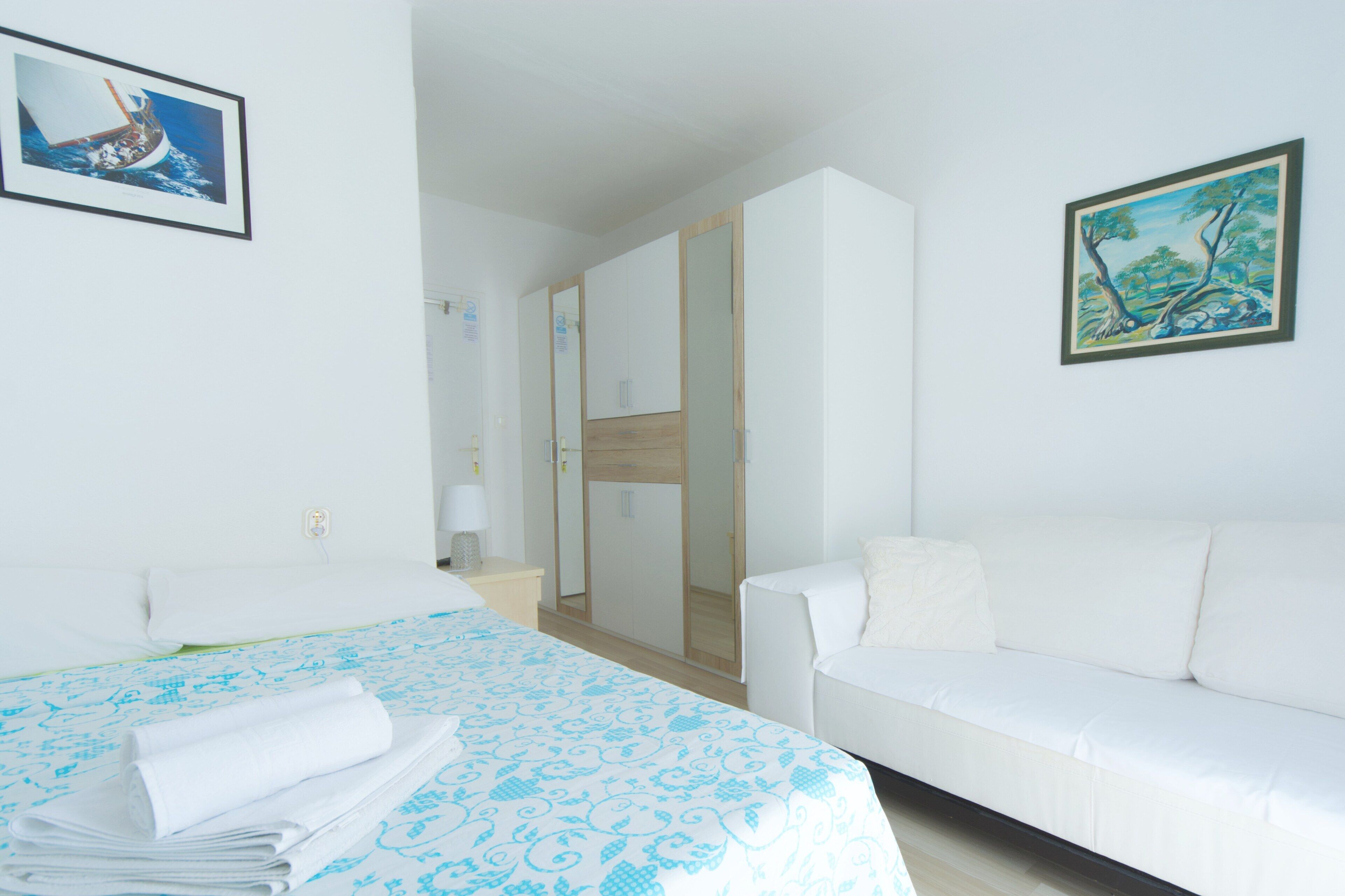 Una habitación de hotel con cama, un sofá blanco, un armario de madera y dos cuadros en las paredes.