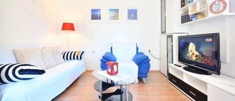 A modern living room with a sofa, a red lamp, a small table, a blue chair, and a TV on a white cabinet.