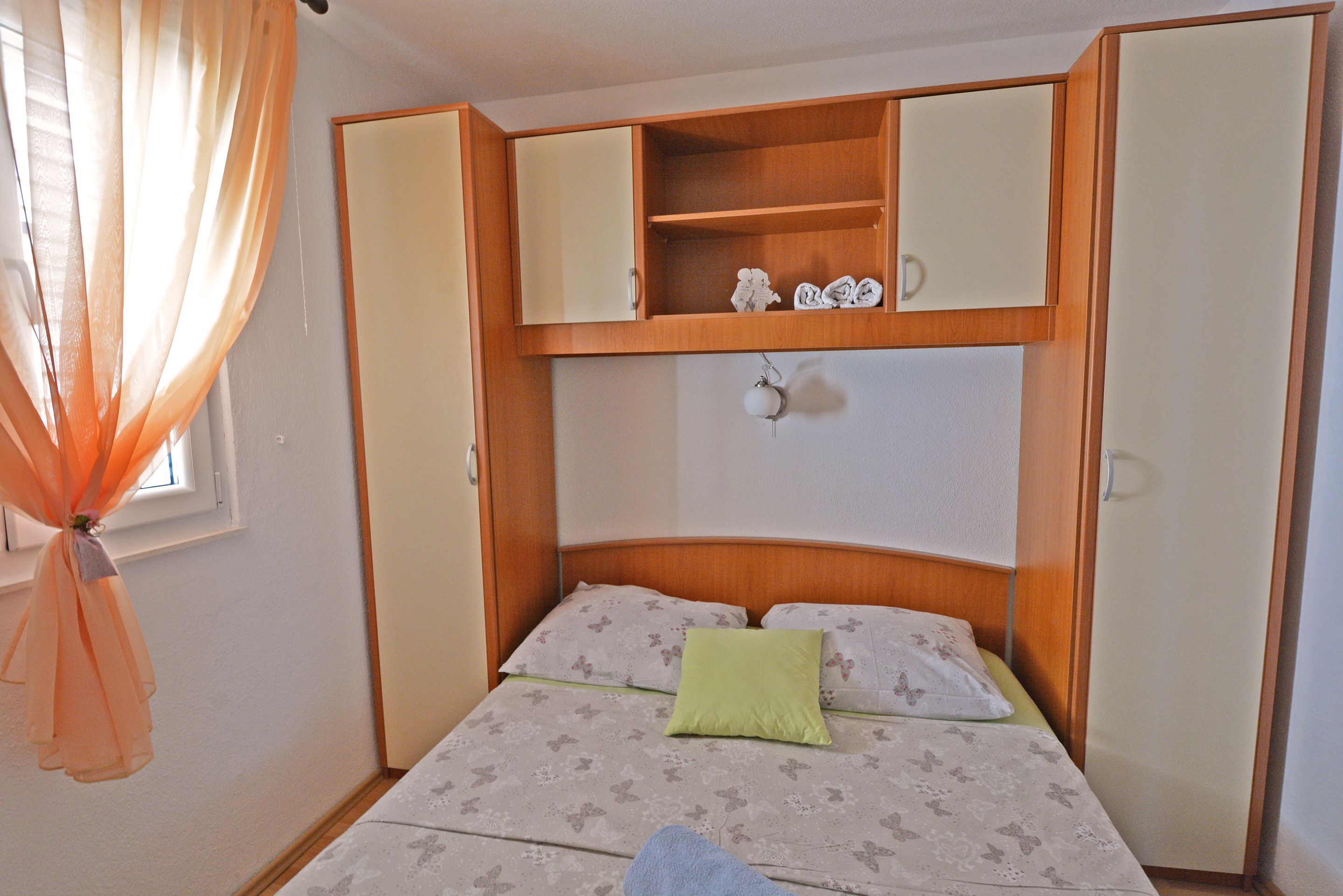 A bedroom with a bed, a nightstand, a wardrobe, and a window with curtains.