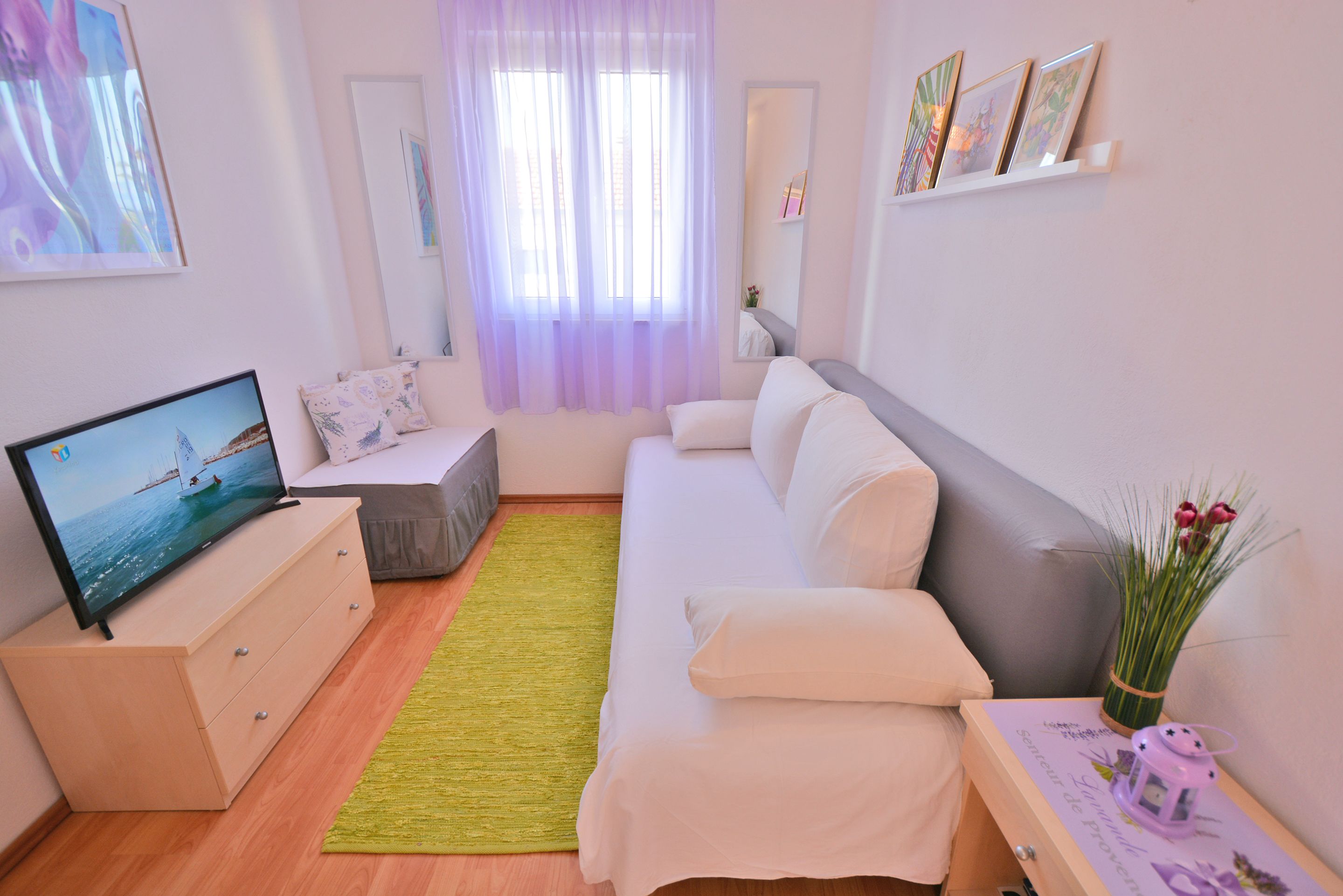 A modern living room with a sofa, a television, a small table with a vase, and a green rug.