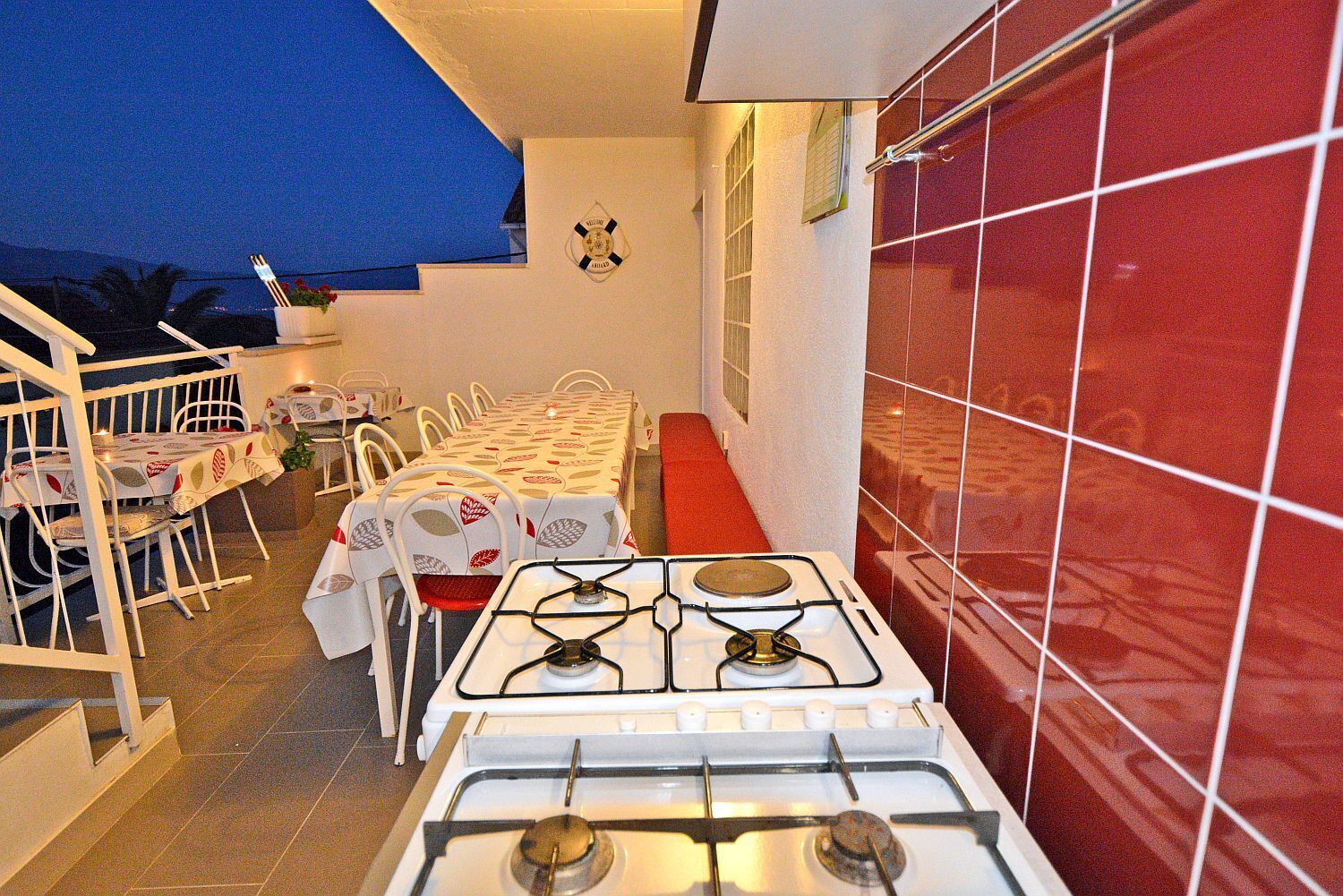 A kitchen with a gas stove, white chairs, and a red tiled wall.
