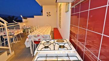 A kitchen with a gas stove, white chairs, and a red tiled wall.