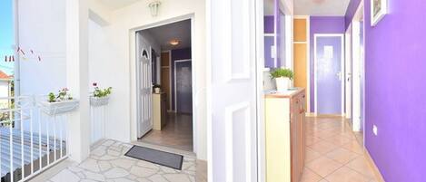 A hallway with a stone floor leading to a door, a small plant on a counter, and a purple wall.
