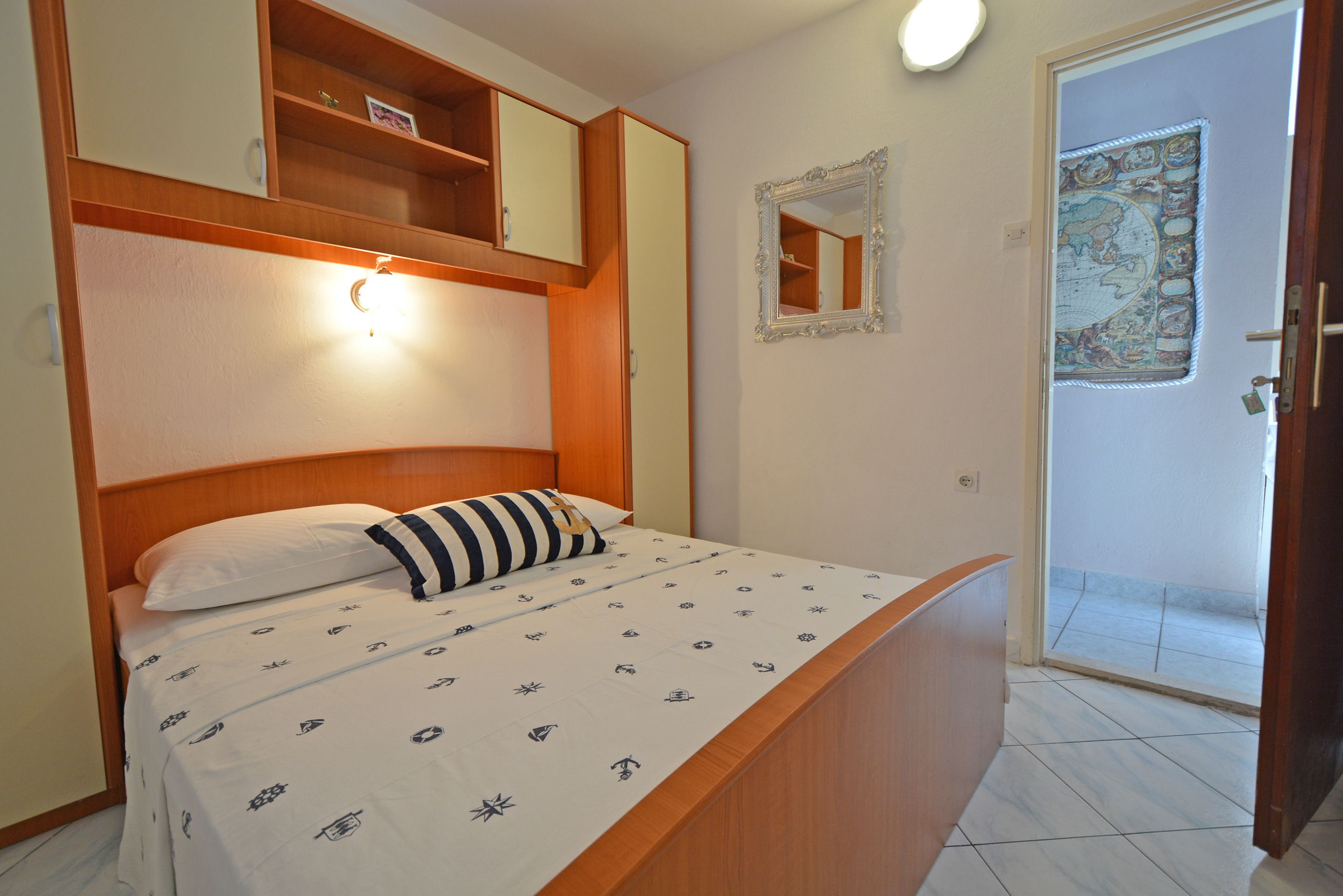A bedroom with a bed, wooden headboard, a nightstand, a mirror, and a door leading to a balcony.