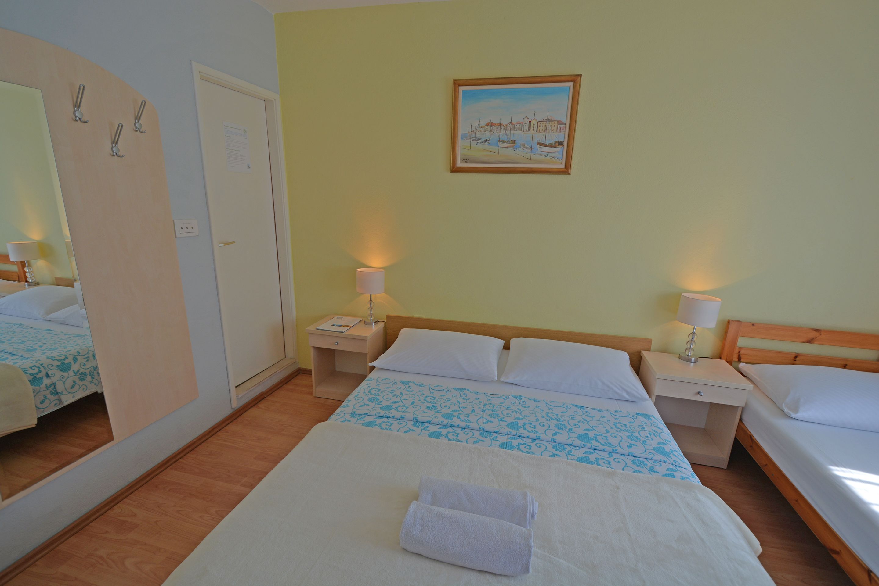 A hotel room with two beds, a wooden headboard, bedside lamps, a painting on the wall, and a mirror.