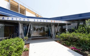 African Beach -hotellin sisäänkäynti, jossa on katettu käytävä ja lasiovet.