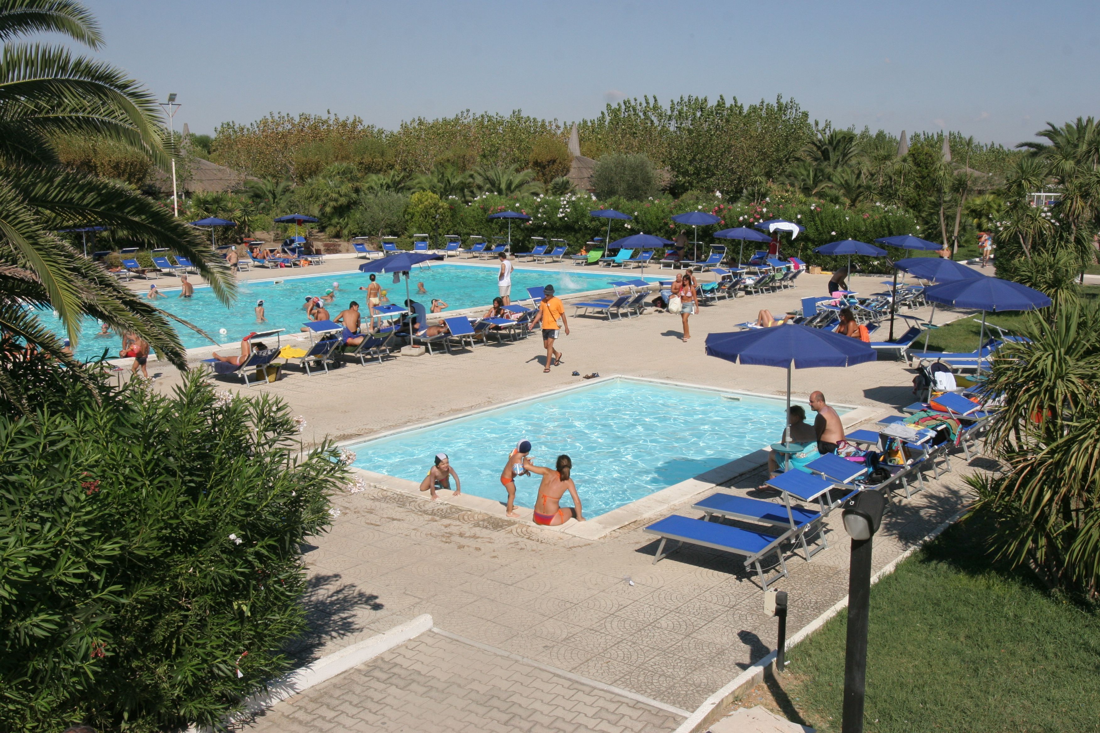 Ein Poolbereich mit mehreren Schwimmbecken, Liegestühlen und Sonnenschirmen.