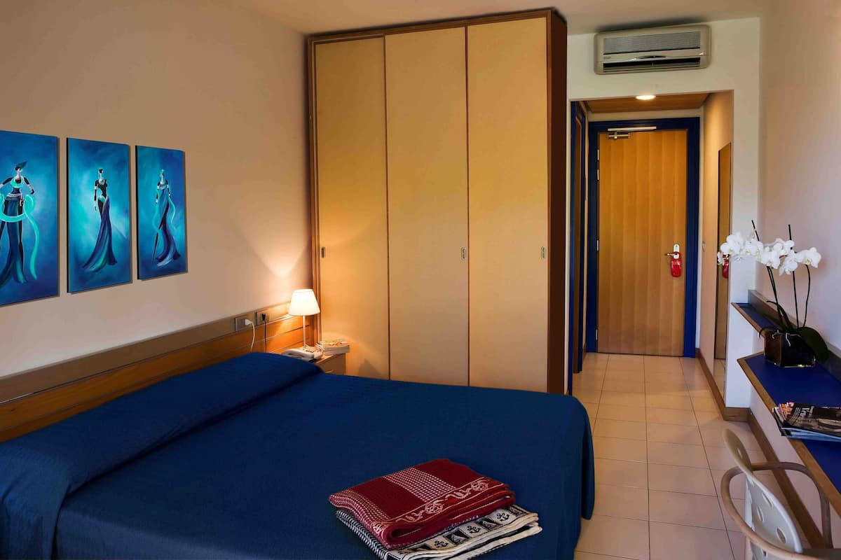 Una habitación de hotel con cama, escritorio, armario y tres cuadros en la pared.