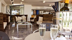 Ein moderner Lounge-Bereich mit Rattanmöbeln, einem Glastisch und einer Bar im Hintergrund.