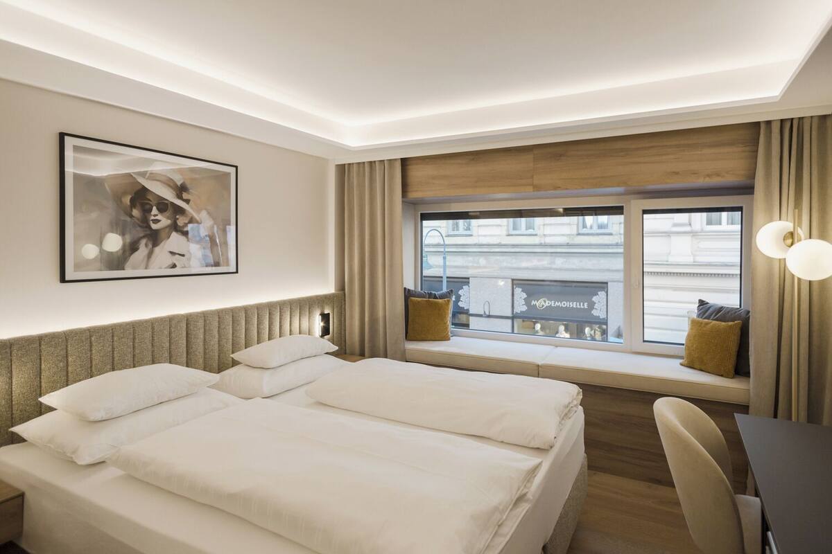 Quarto de hotel com cama grande, escrivaninha e janela com vista para a rua.