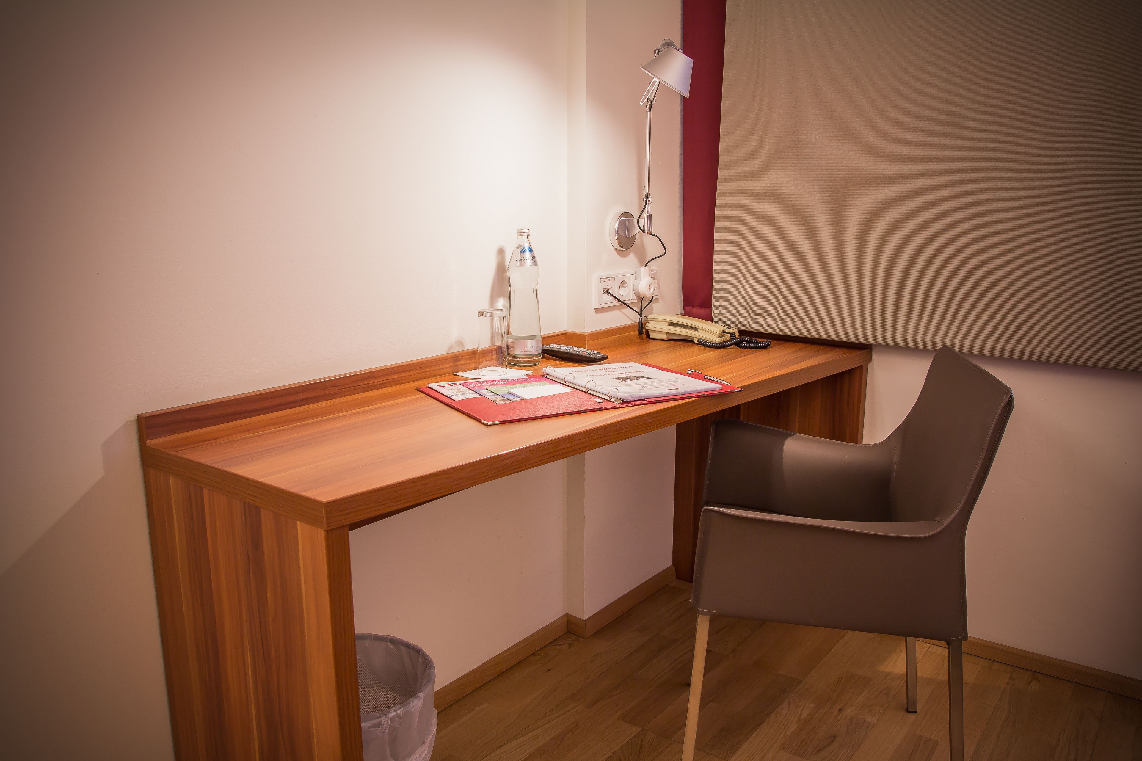 A small wooden desk with a chair, a lamp, a bottle, and some papers.