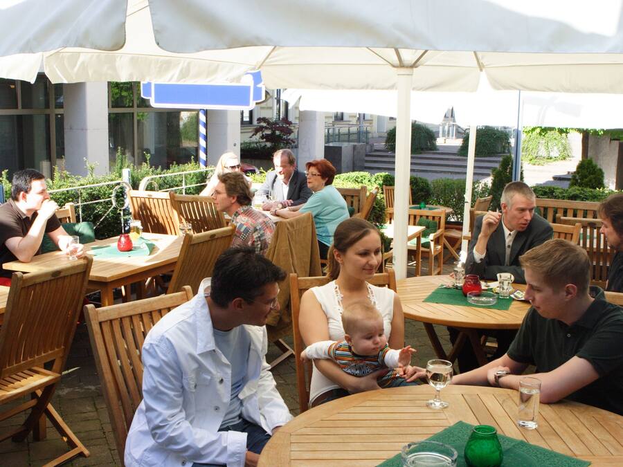 Een terras met houten tafels en stoelen, parasols en een uitzicht op gebouwen op de achtergrond.