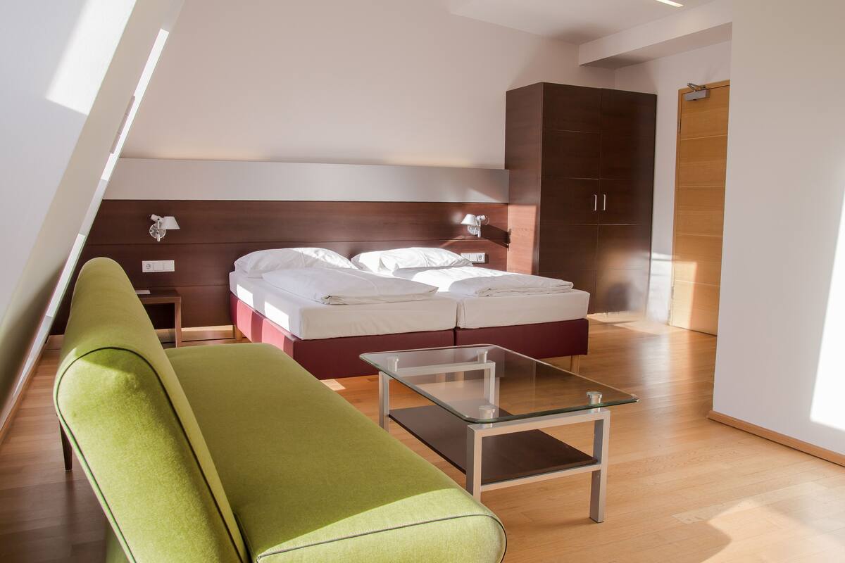 Quarto de hotel moderno com uma cama, um sofá verde, uma mesa de centro de vidro e um guarda-roupa.