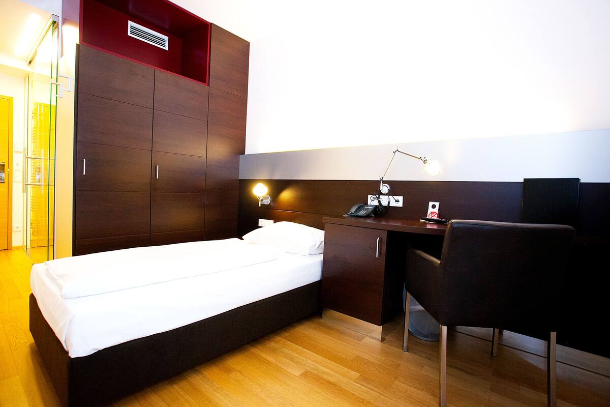 Quarto de hotel com cama, escrivaninha, cadeira e guarda-roupa.