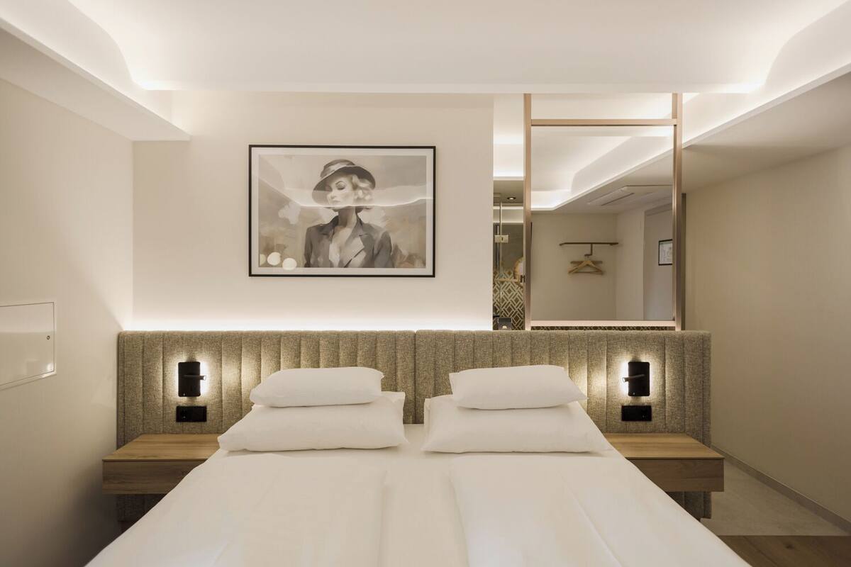 Quarto de hotel moderno com uma cama grande, duas mesas de cabeceira, um quadro na parede e um espelho.