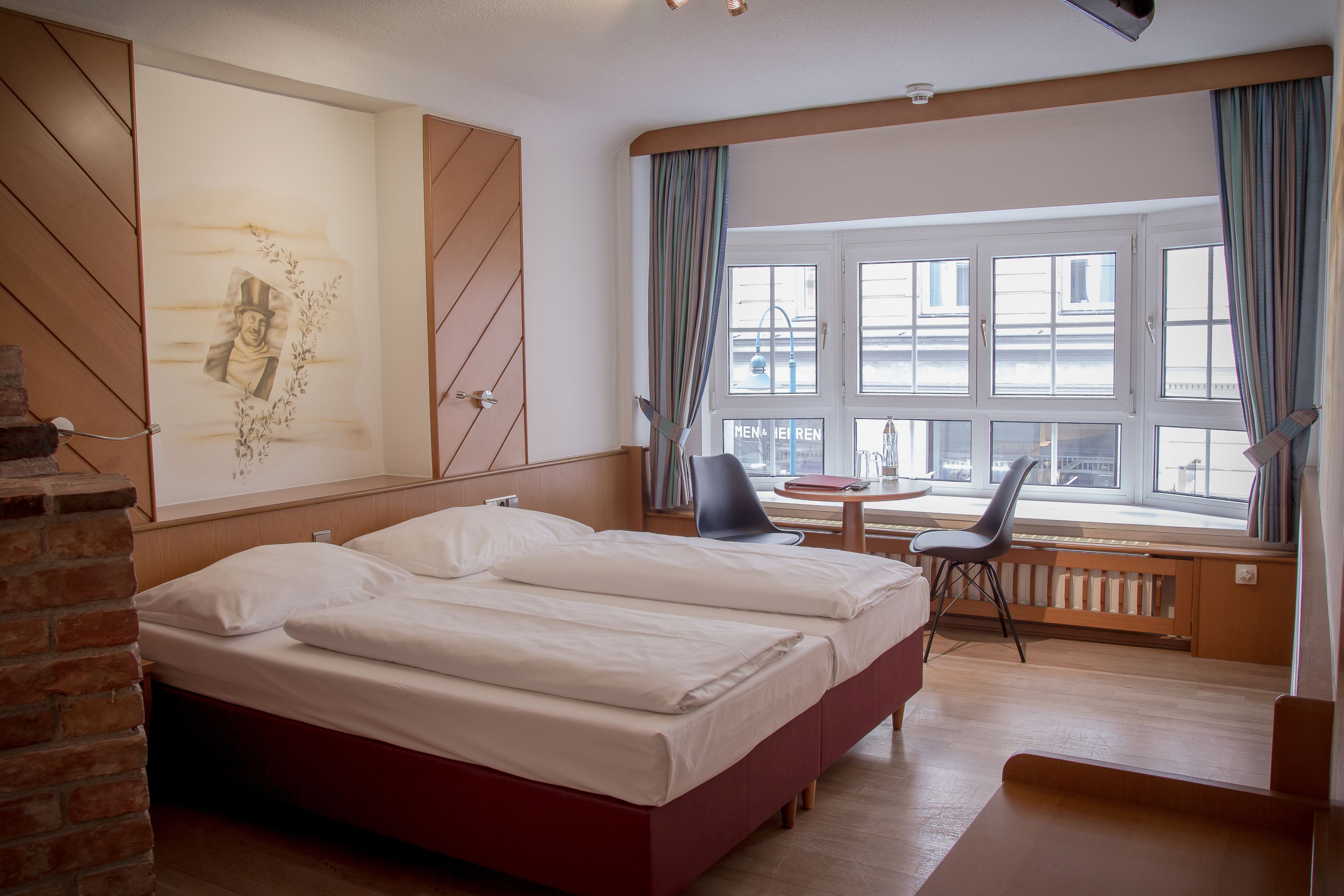 Habitación de hotel con una cama grande, un escritorio con silla, una ventana con cortinas y un radiador.