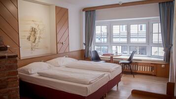 Habitación de hotel con una cama grande, un escritorio con silla, una ventana con cortinas y un radiador.