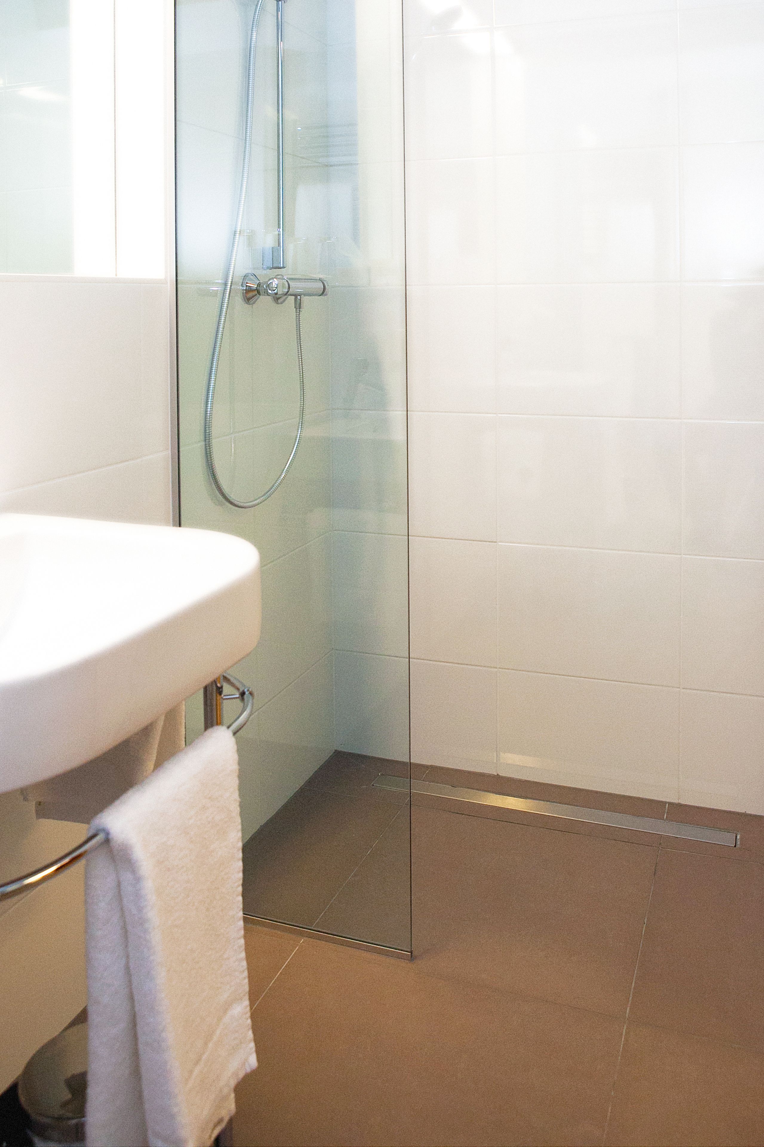 A bathroom with a glass shower enclosure, a white sink, and a towel rack.