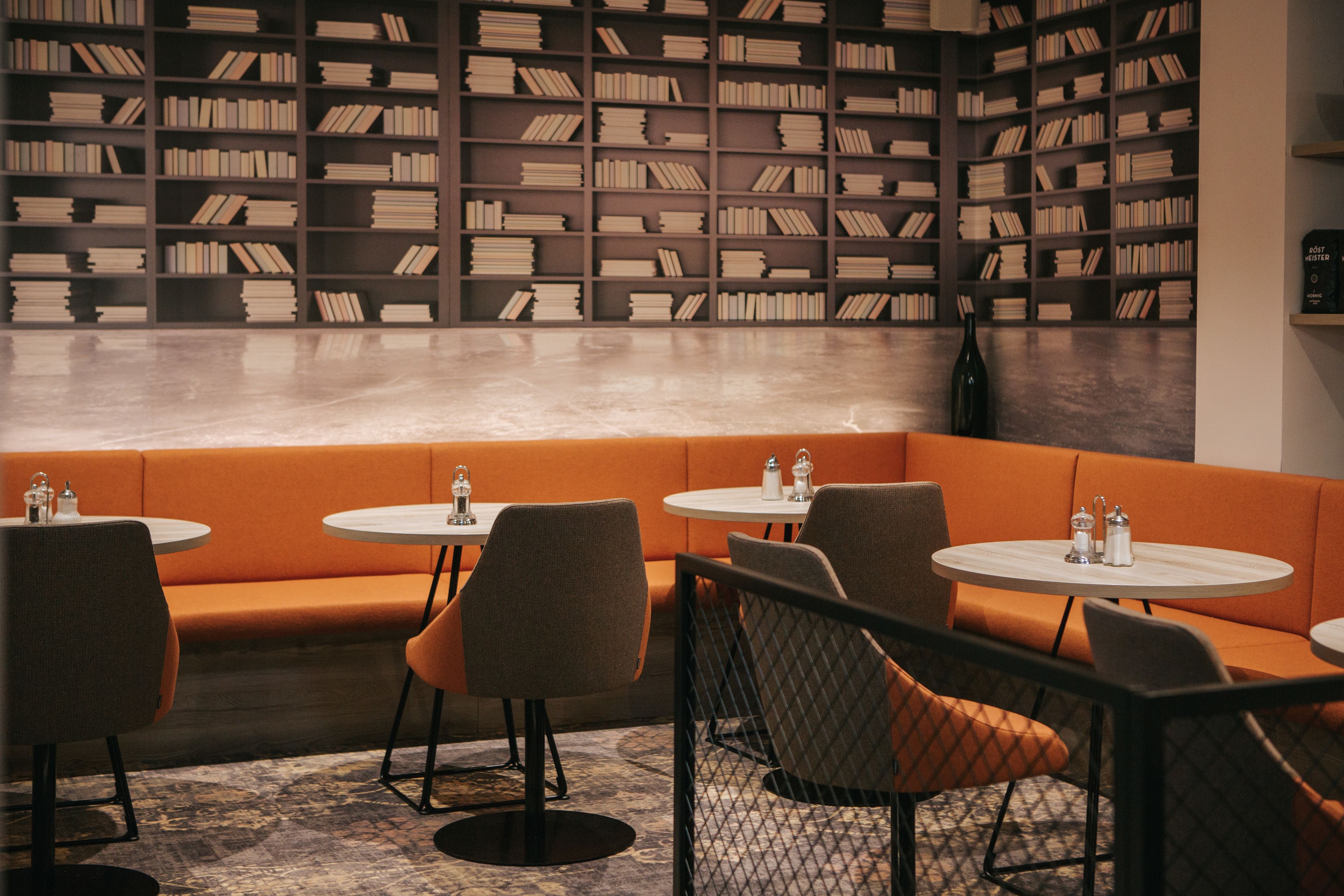A library-style seating area with bookshelves, orange seating, and round tables.