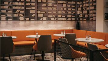 A library-style seating area with bookshelves, orange seating, and round tables.