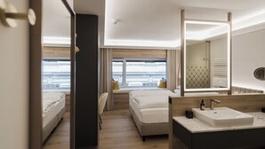 A modern hotel room with a large bed, a smaller bed, a sitting area, and a bathroom with a large mirror and sink. - Hotel Schwarzer Bär (Linz)