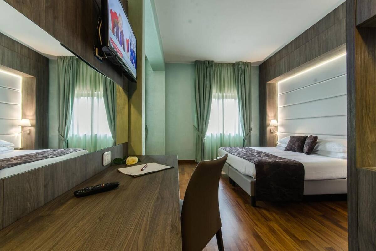 Een hotelkamer met een houten vloer, twee bedden, een bureau met afstandsbediening en een aan de muur bevestigde televisie.