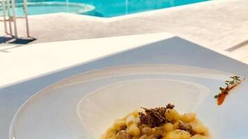 Et spisebord med en tallerken pasta i et udendørs miljø med en pool i baggrunden.