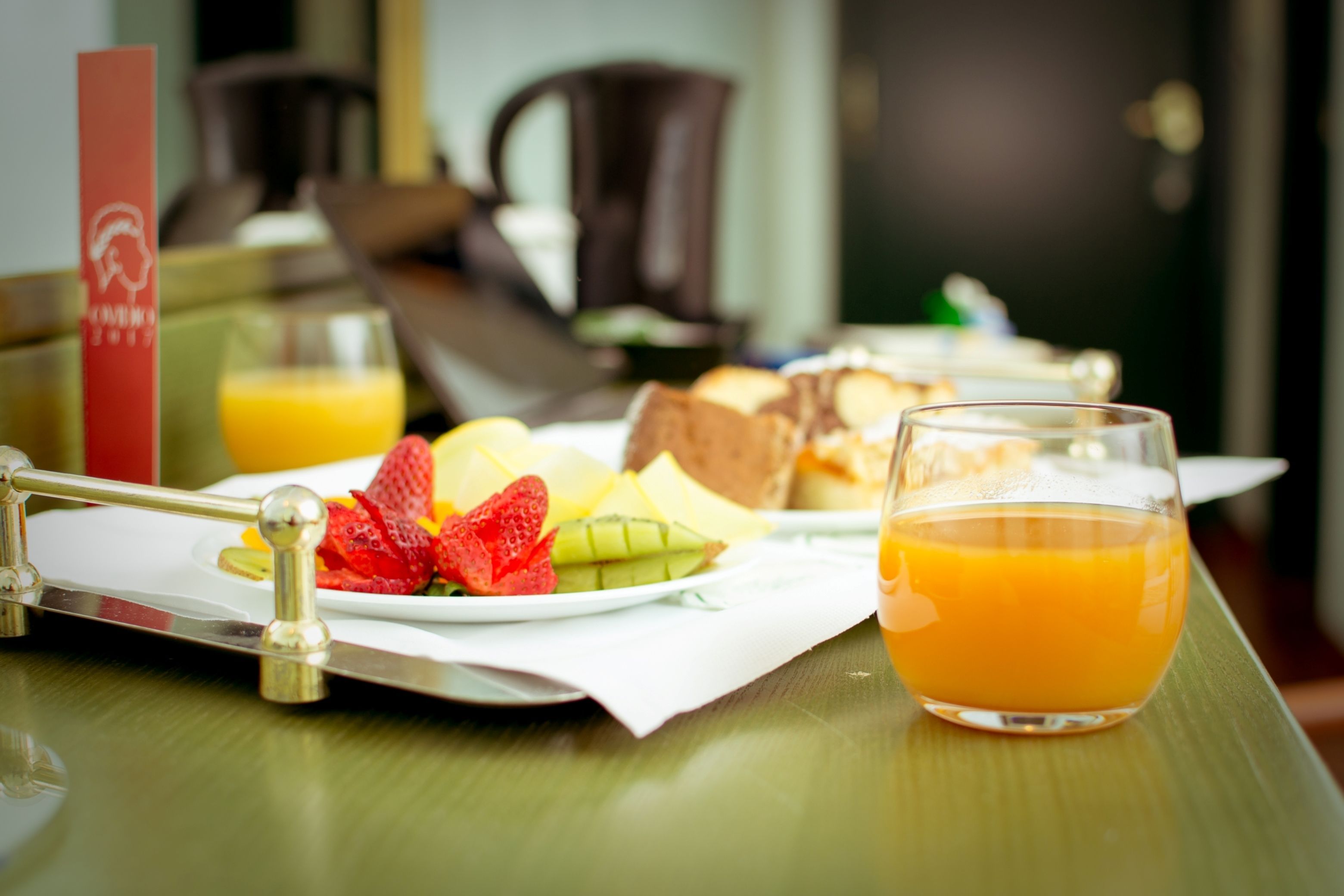 Bandeja de desayuno con diferentes alimentos y un vaso de jugo de naranja sobre una mesa de madera.
