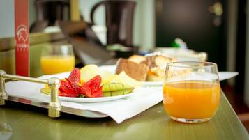 Bandeja de desayuno con diferentes alimentos y un vaso de jugo de naranja sobre una mesa de madera.