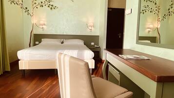 A hotel room with a bed, a desk, a chair, and a mirror.
