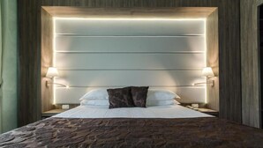Ein modernes Schlafzimmer mit einem großen Bett, zwei Nachttischlampen und einem Kopfteil mit integrierter Beleuchtung.