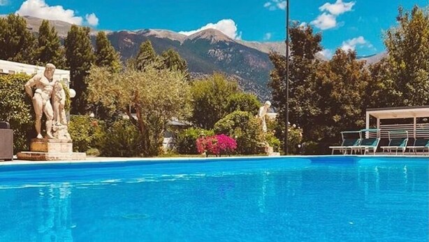 Ein Schwimmbecken mit einer Statue, umgeben von viel Grün und Bergen im Hintergrund.