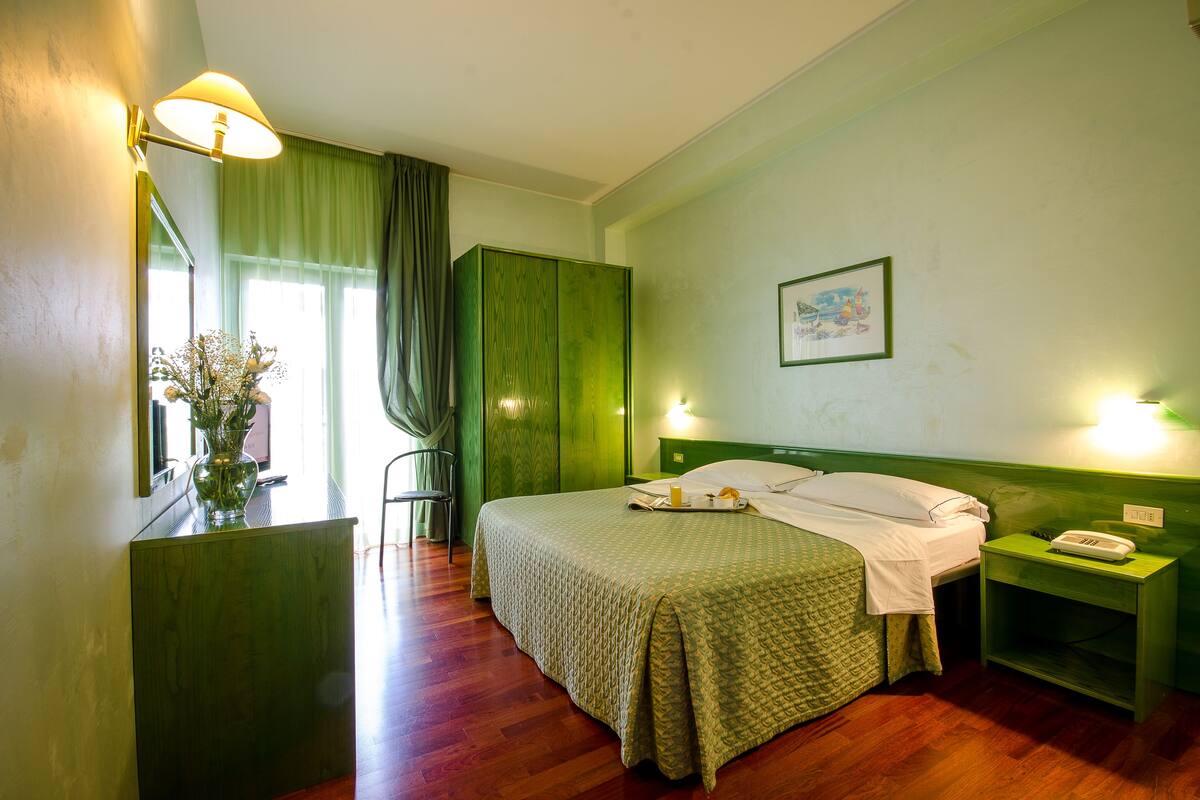 Een hotelkamer met een bed, een nachtkastje met een telefoon, een bureau met een lamp en een stoel.