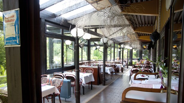 An indoor dining area with tables and chairs, large windows, and hanging light fixtures. - Parkhotel Hitzacker (Hitzacker)