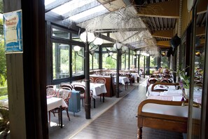 Un comedor interior con mesas y sillas, ventanas amplias y lámparas colgantes.