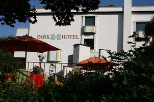 Un hotel llamado "Park Hotel" con fachada blanca, un balcón y sombrillas de exterior.