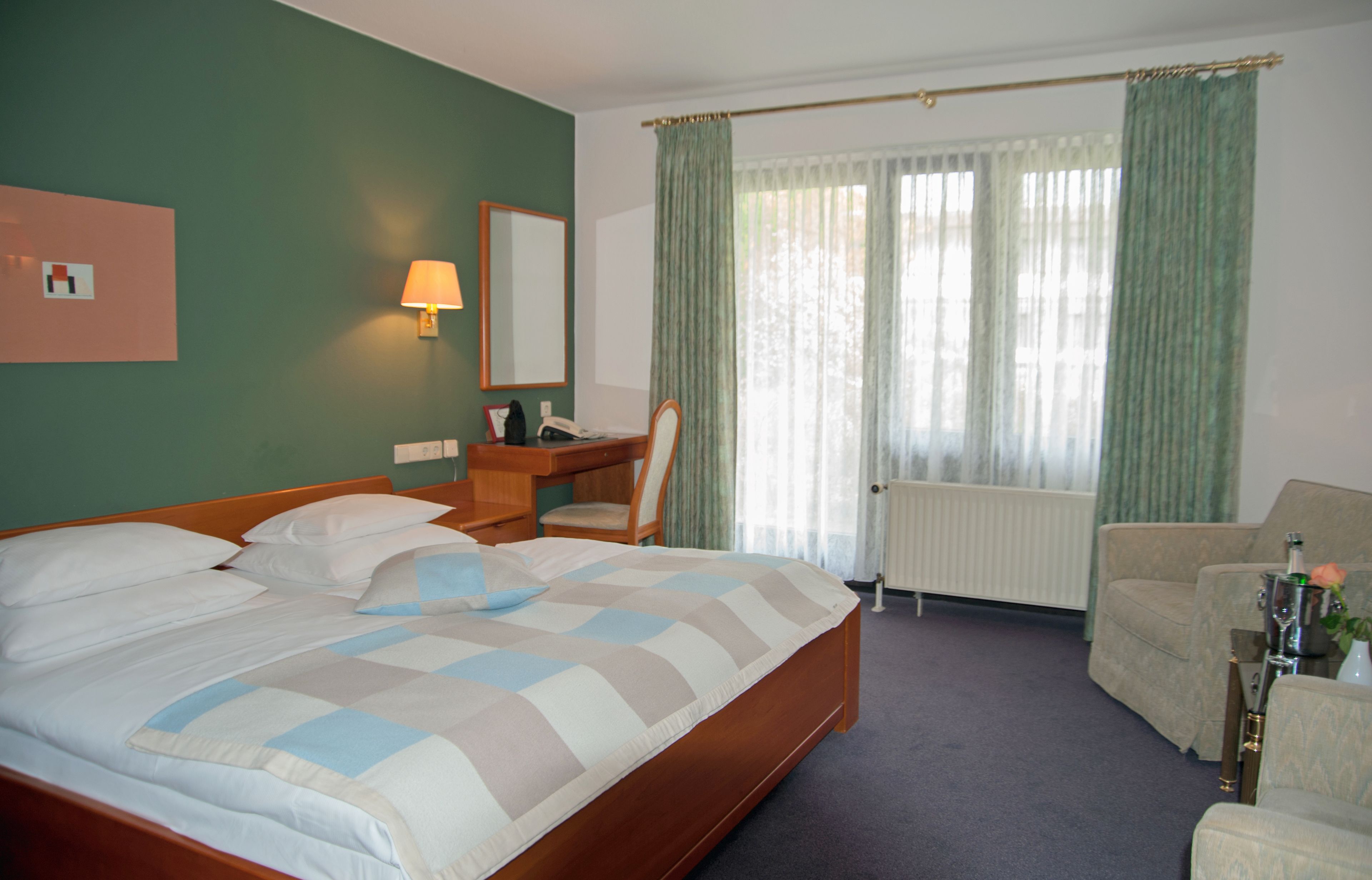 A hotel room with a large bed, a desk with a lamp, a chair, and a sofa.