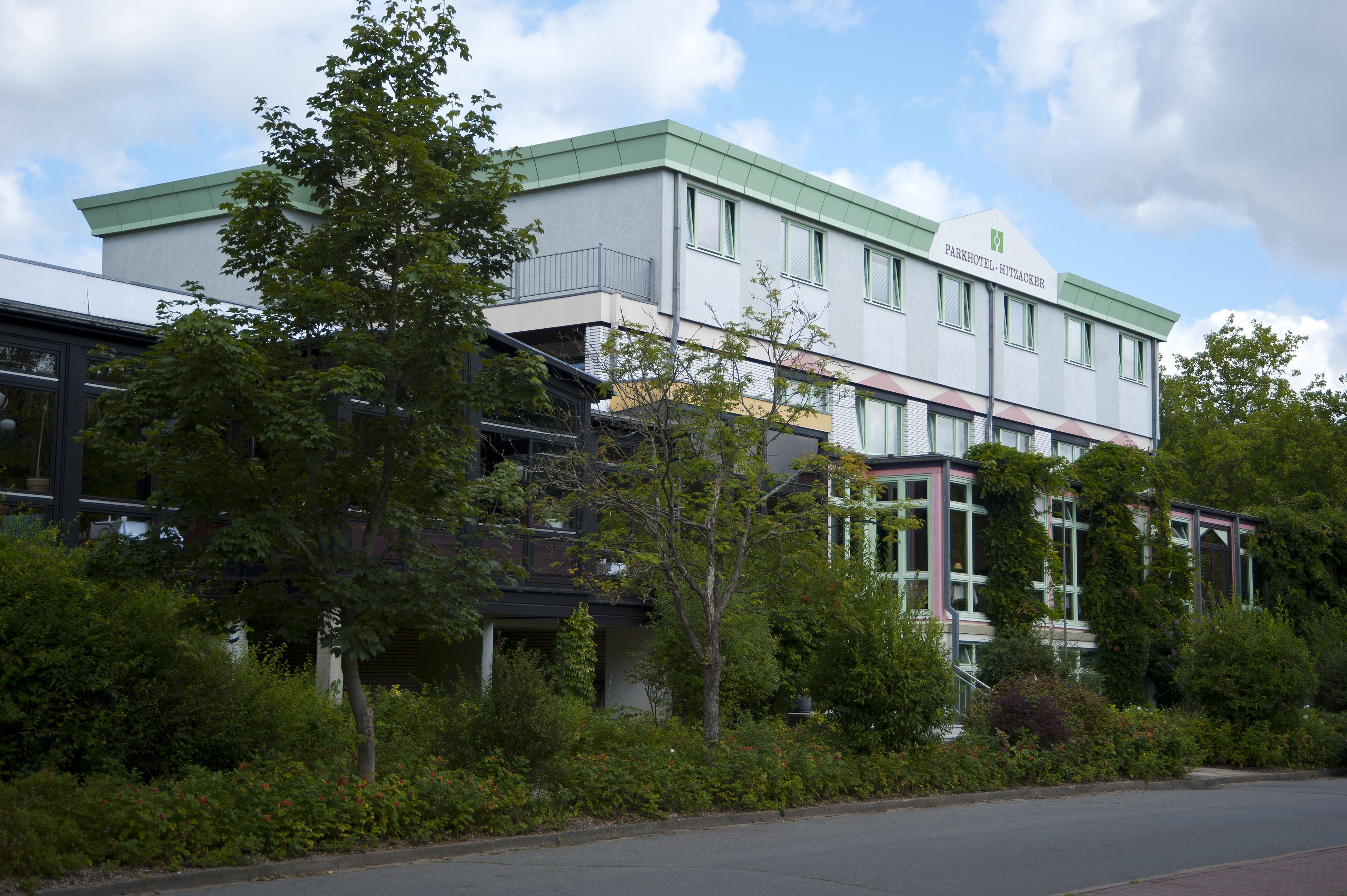 A modern hotel with a flat roof, large windows, and a green sign.