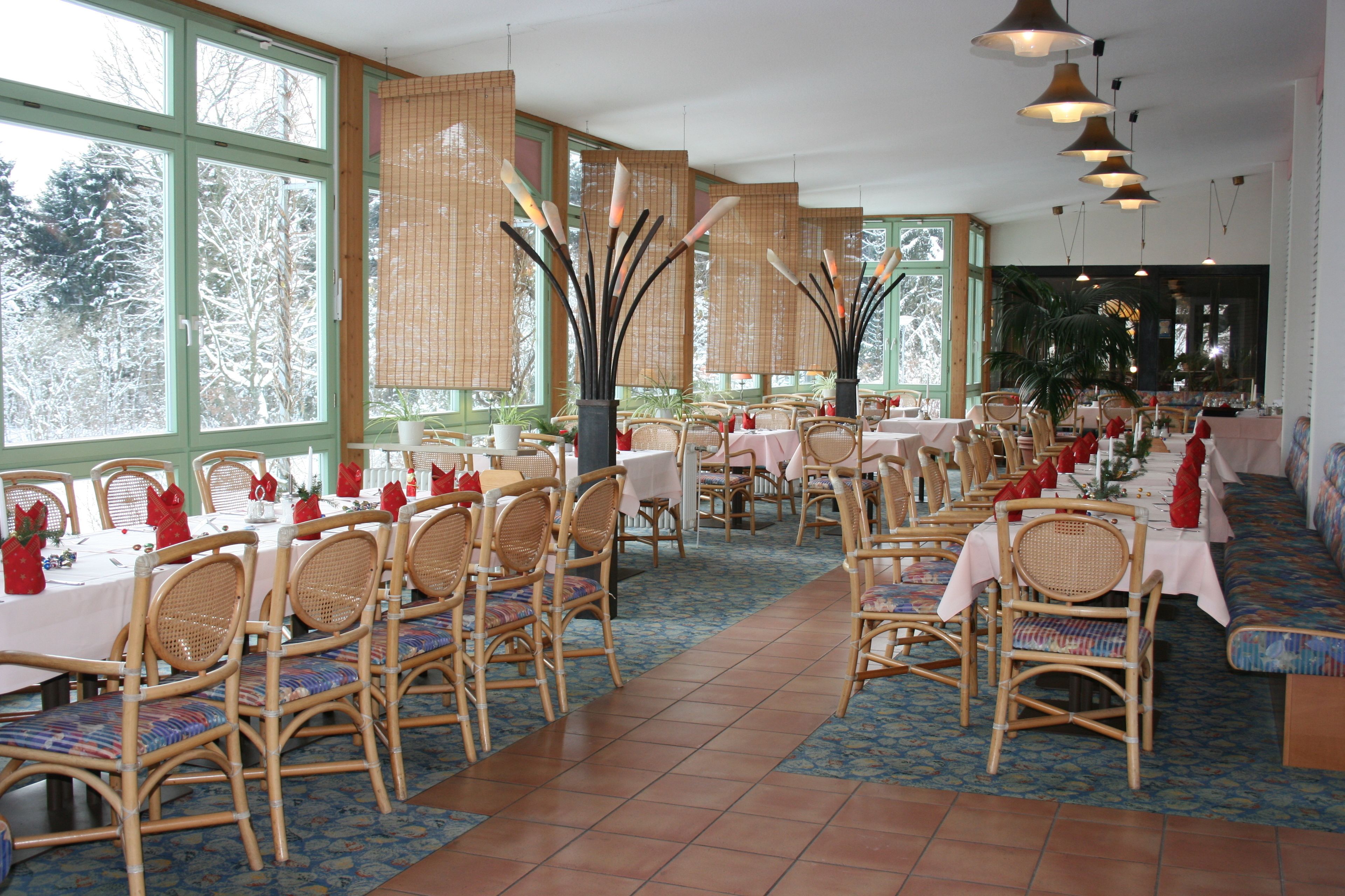 Un restaurant doté de nombreuses tables et chaises, de grandes fenêtres et de luminaires suspendus.
