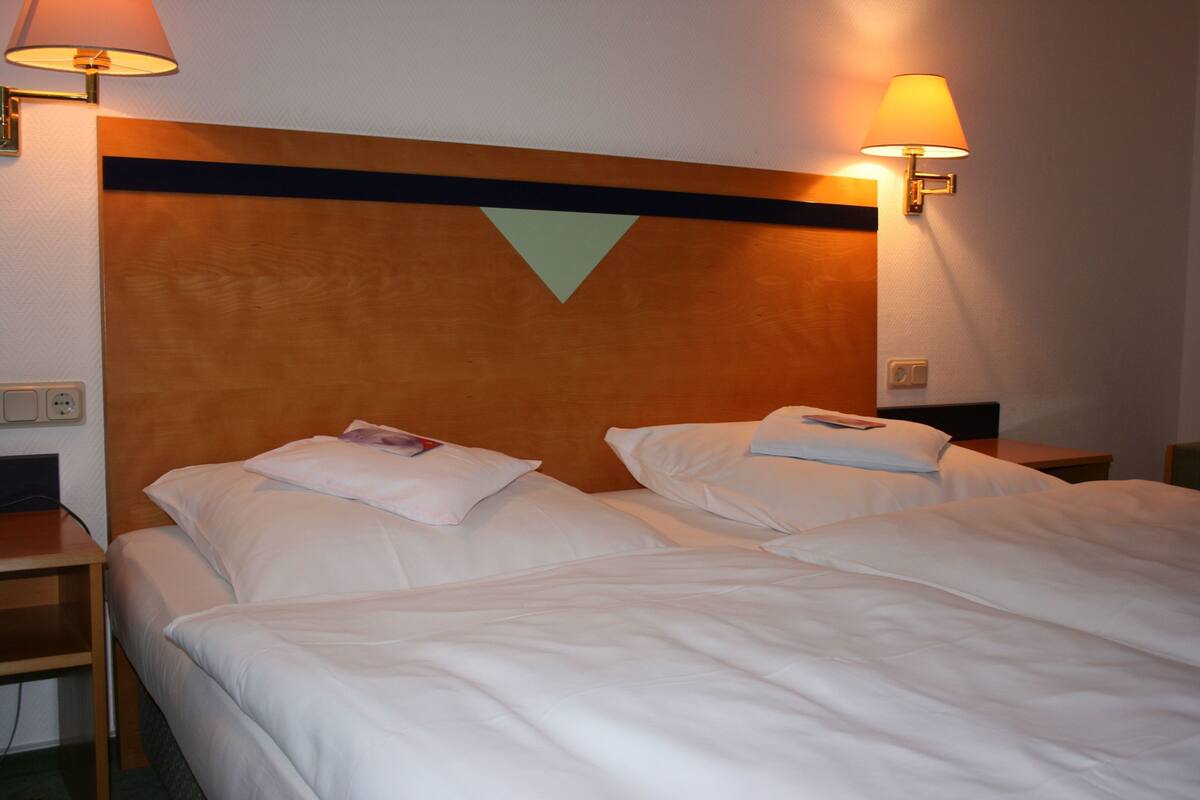 Una habitación de hotel con dos camas, cabecero de madera y lámparas fijadas a la pared.