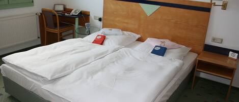 Habitación de hotel con cama doble, escritorio con silla, teléfono y mesita de noche con lámpara.