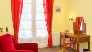 A room with a red chair, a wooden desk, a small table with a vase, and a chandelier.