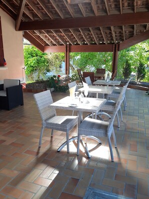 An outdoor patio with a covered seating area, featuring tables and wicker chairs, surrounded by potted plants and a stone wall. - Hostellerie de la Roseraie (Cazaubon)