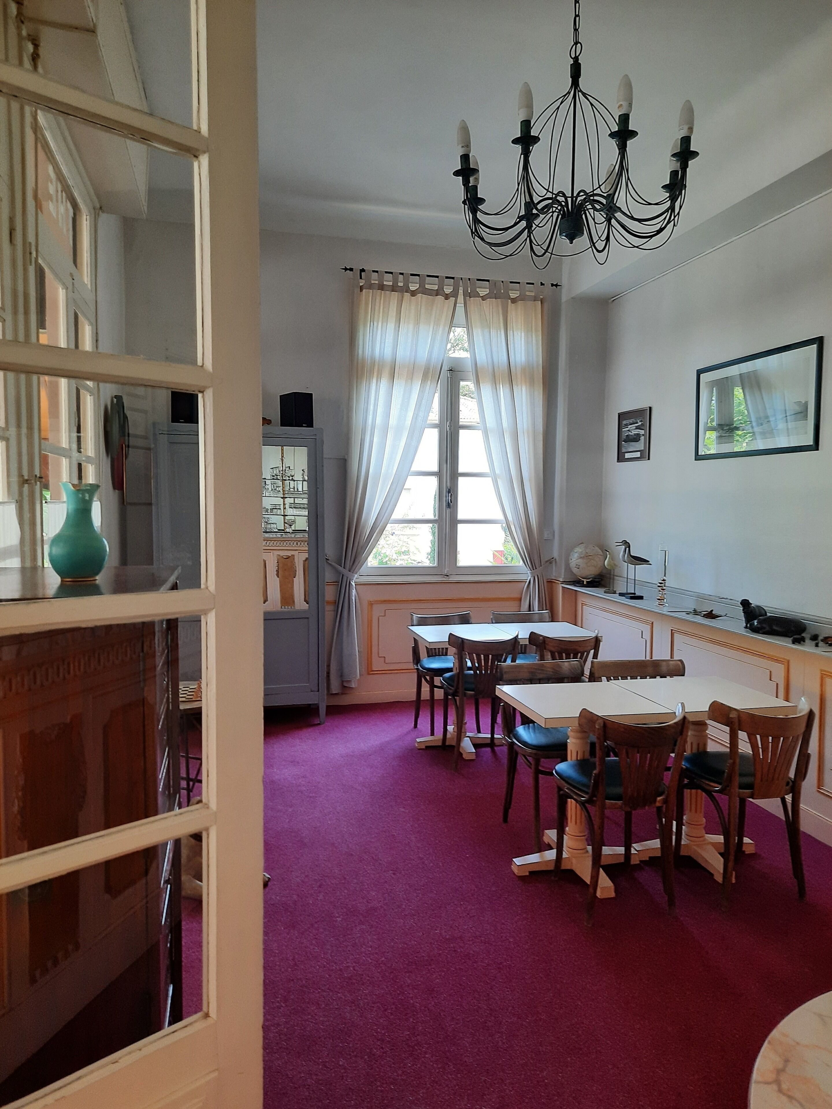 Un comedor con una mesa, sillas, una araña y una ventana con cortinas.