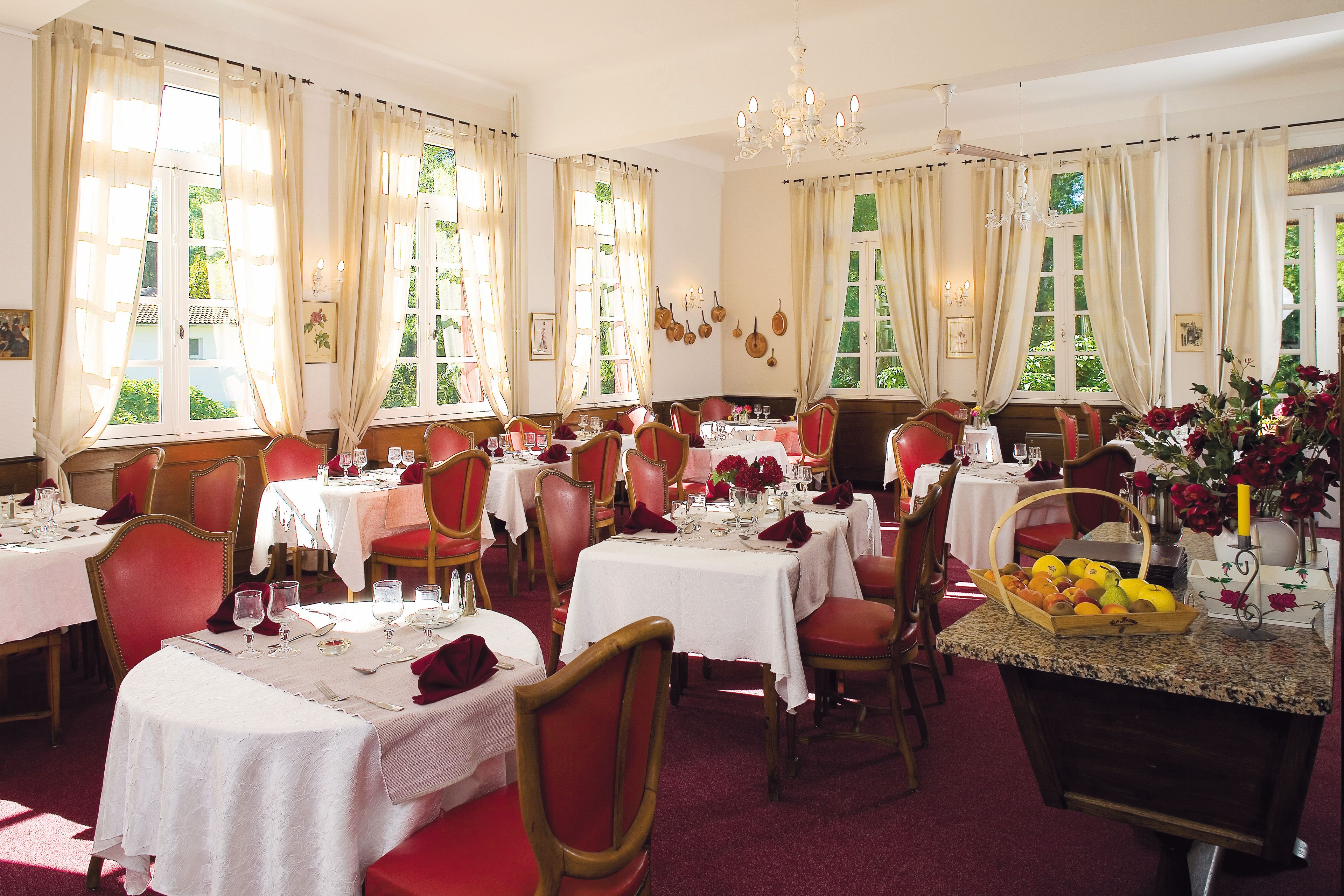 A dining area with multiple tables set for a meal, red chairs, and a chandelier.