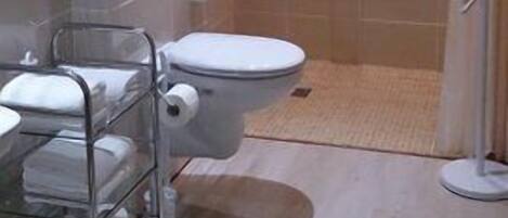 Un baño con inodoro, ducha y lavamanos con toallero.