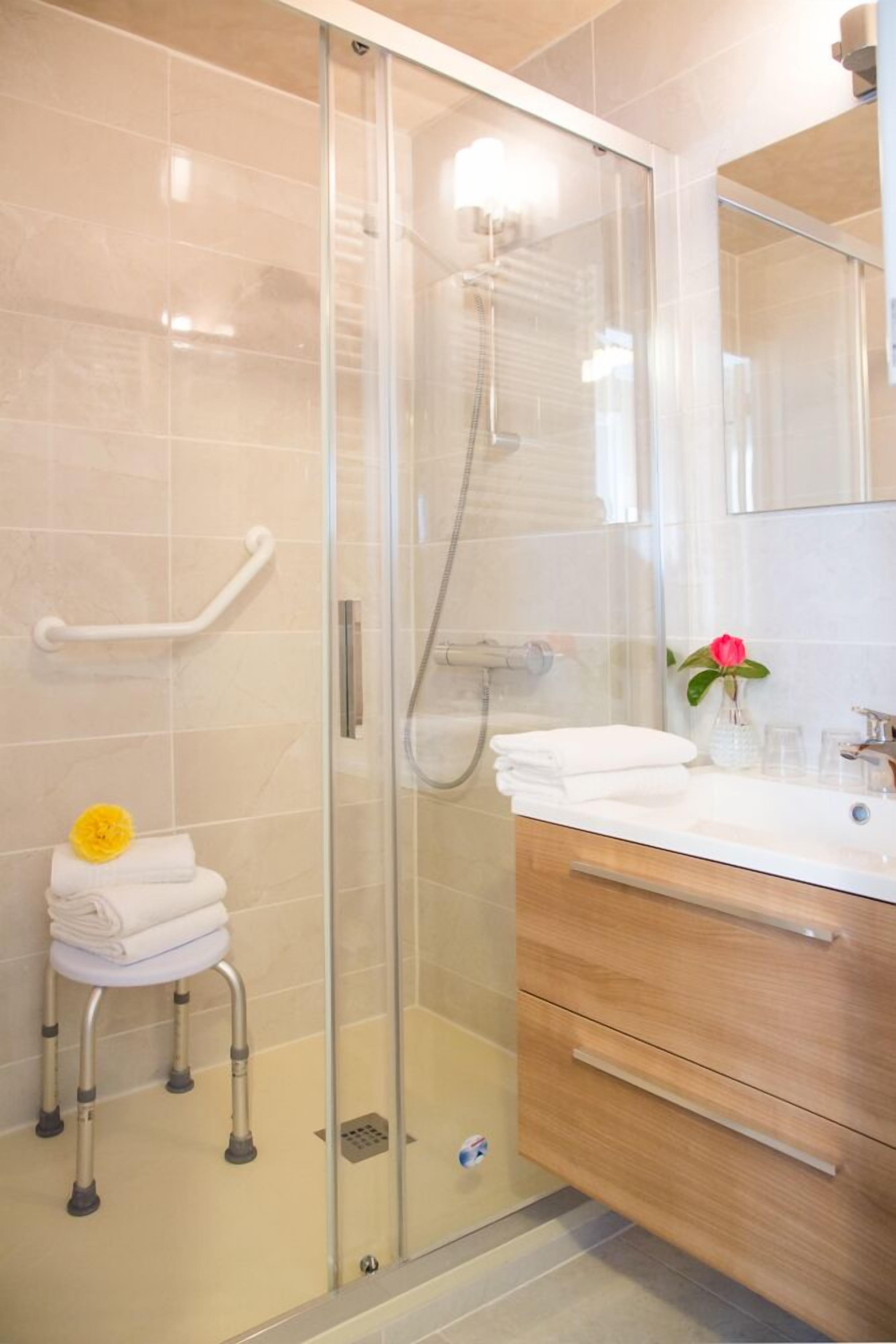Un baño moderno con cabina de ducha de vidrio, inodoro blanco y un tapete de baño amarillo, además de un tocador de madera con espejo.